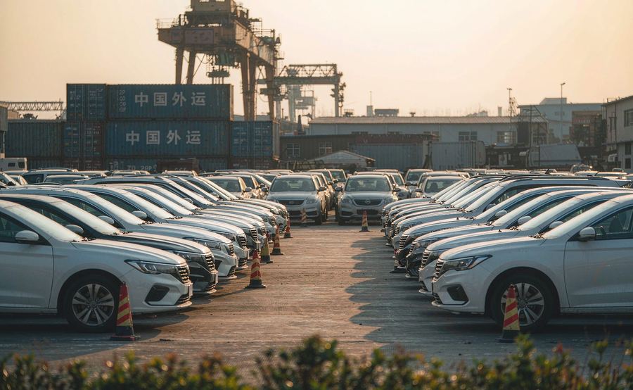 Used cars lined up at an export yard in Guangzhou with shipping containers behind